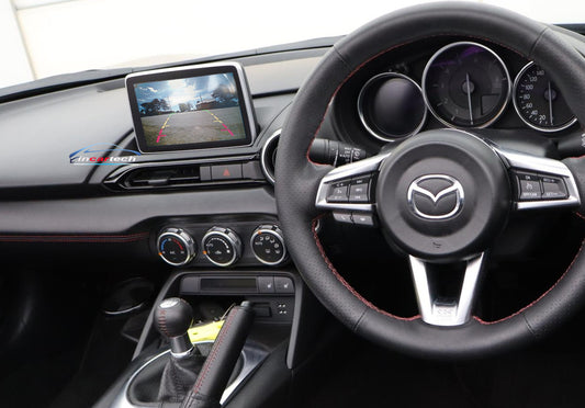 Car interior with steering wheel and dashboard, featuring a Mazda logo.