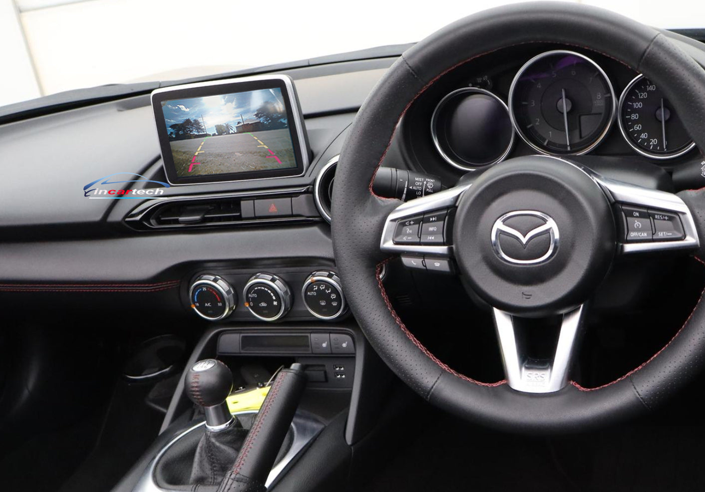 Car interior with steering wheel and dashboard, featuring a Mazda logo.
